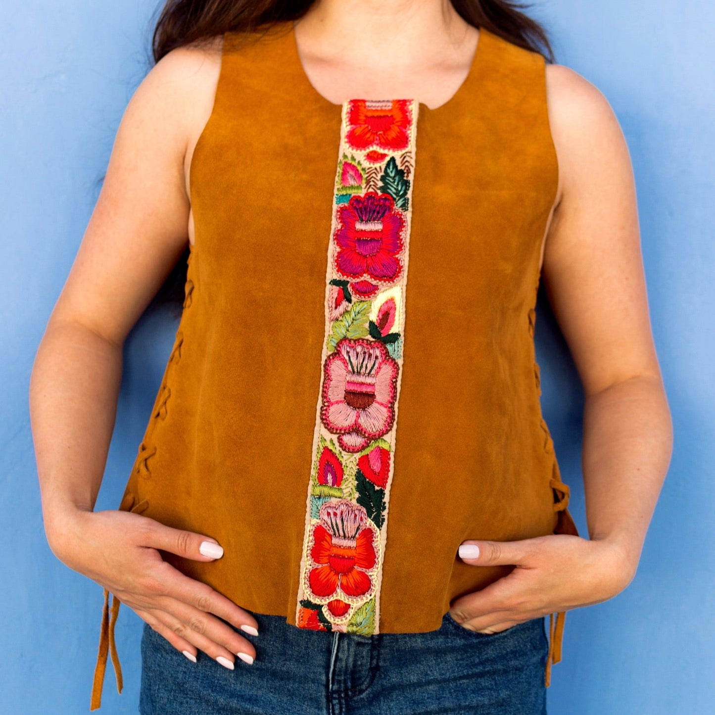 Woman wearing a mustard yellow sleeveless top with a colorful floral band against a blue background