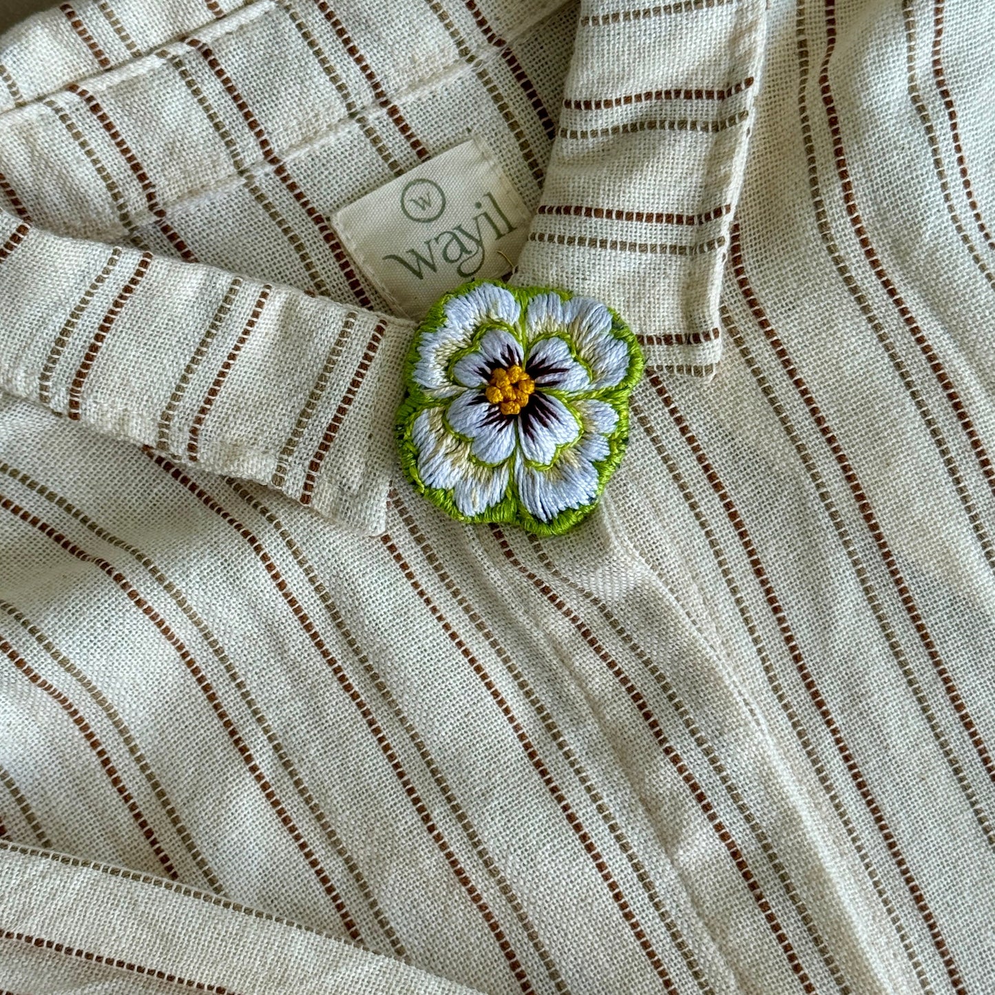Close-up of a striped fabric with a floral brooch on a neutral background