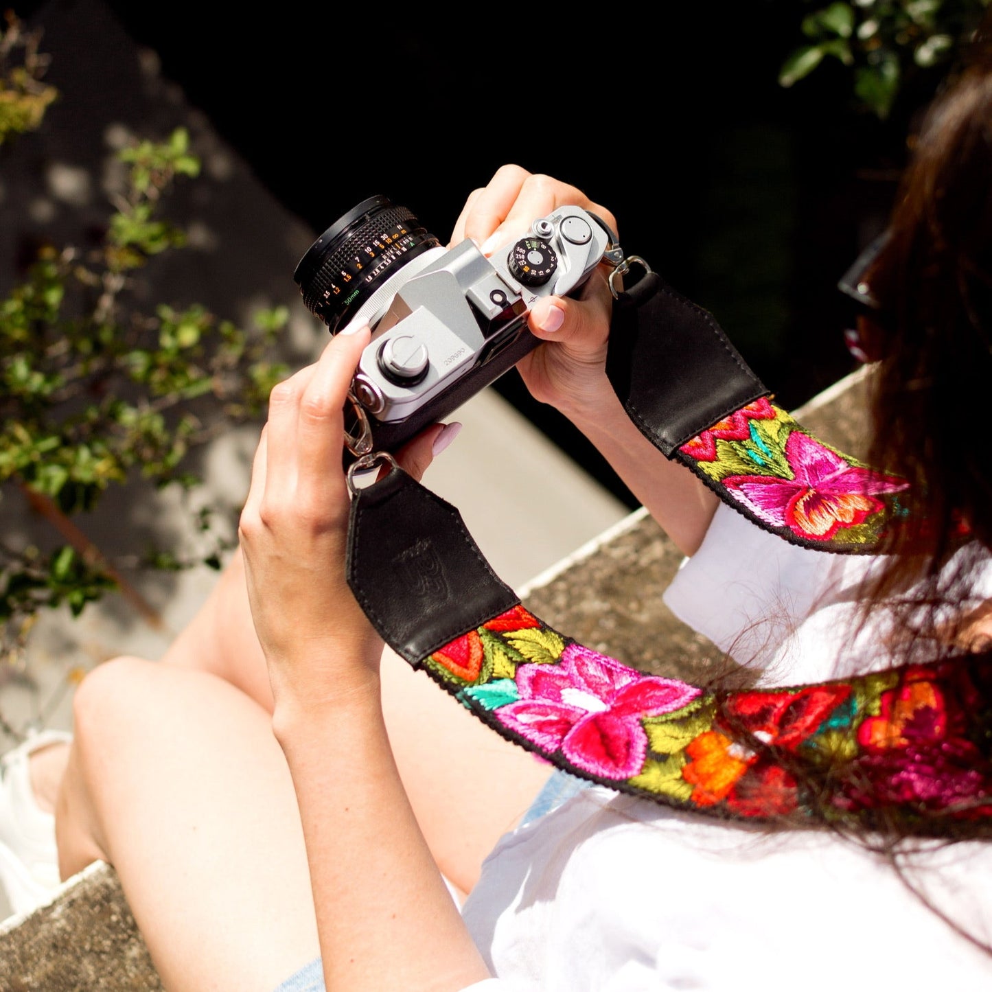 Person holding a camera with a colorful floral strap outdoors