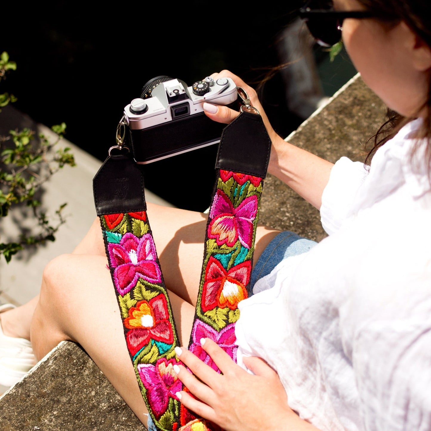 Person holding a camera with a colorful floral strap outdoors.