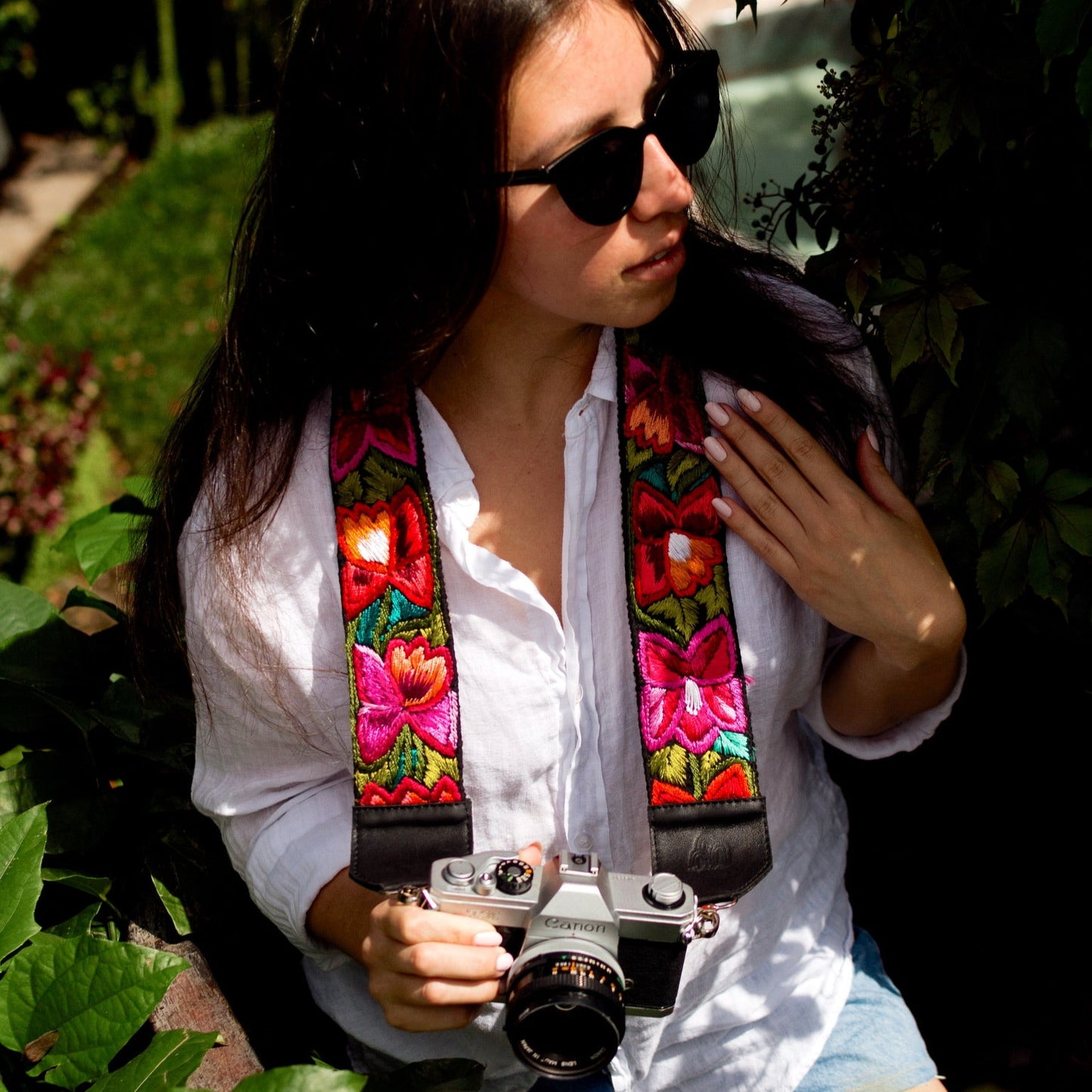 Woman holding a camera with a colorful strap in a garden setting