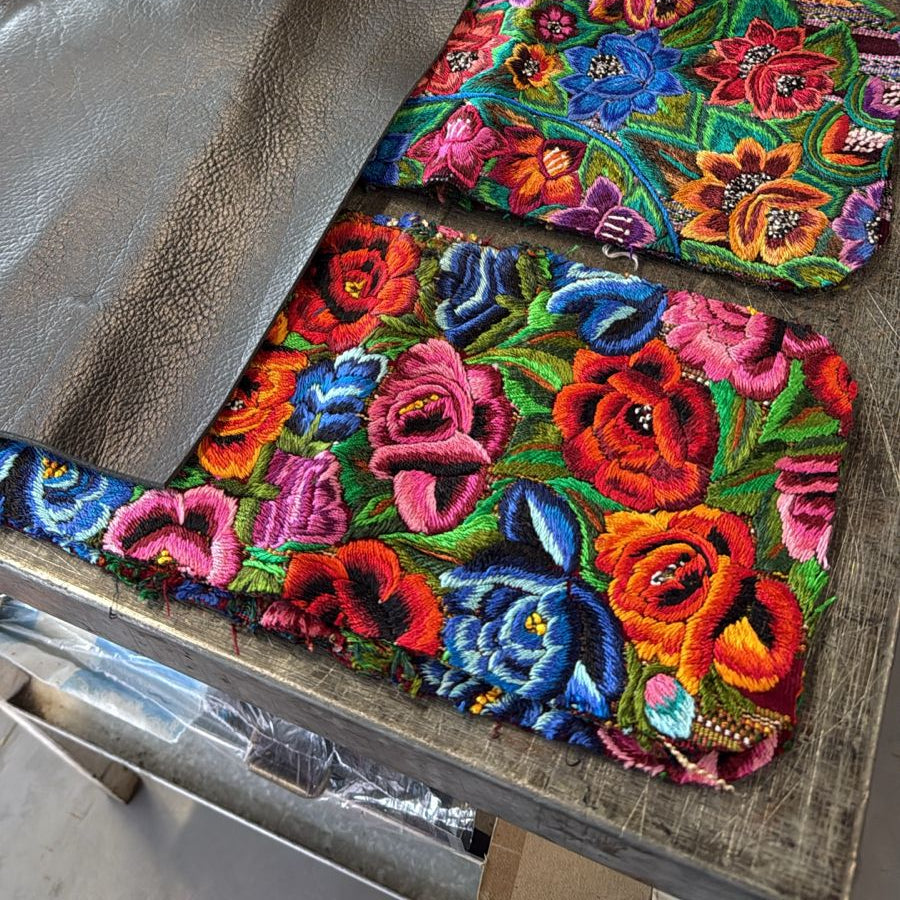 Colorful embroidered fabric on a wooden surface with black leather pieces.