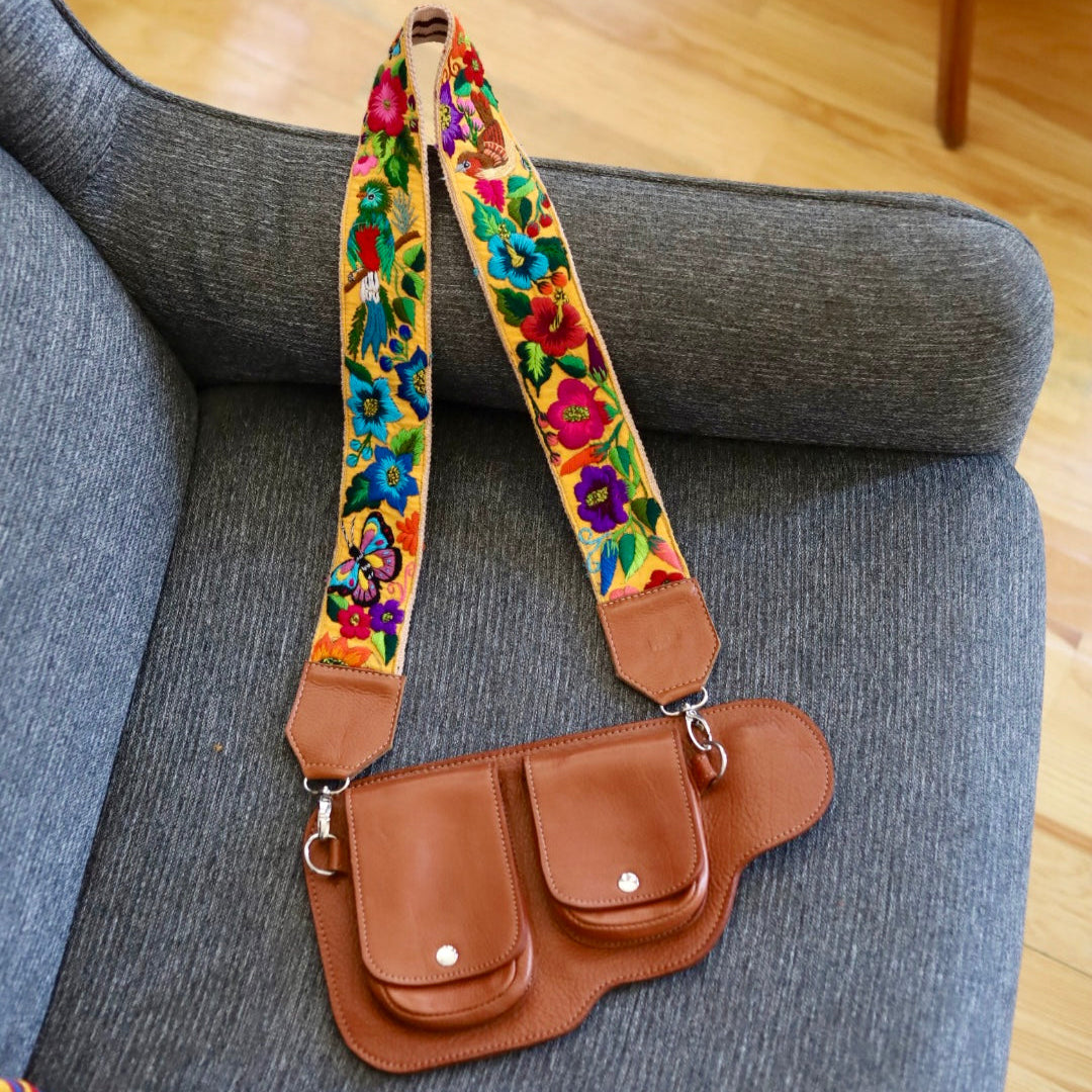 Brown leather bag with colorful floral strap on a gray couch