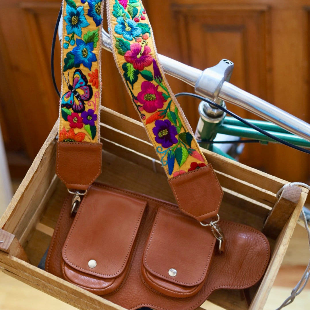 Brown leather bag with a colorful floral strap on a wooden surface.