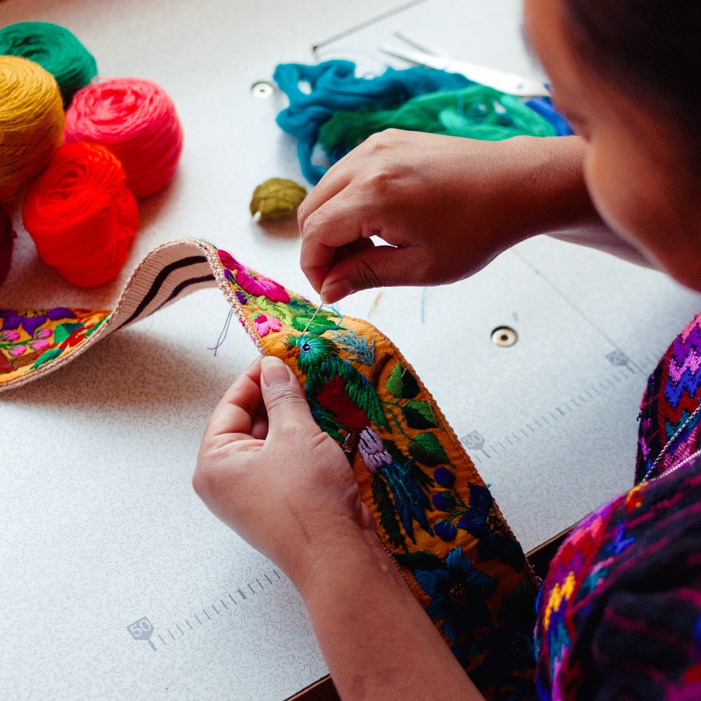 Person working on a colorful craft project with yarn and fabric on a table.