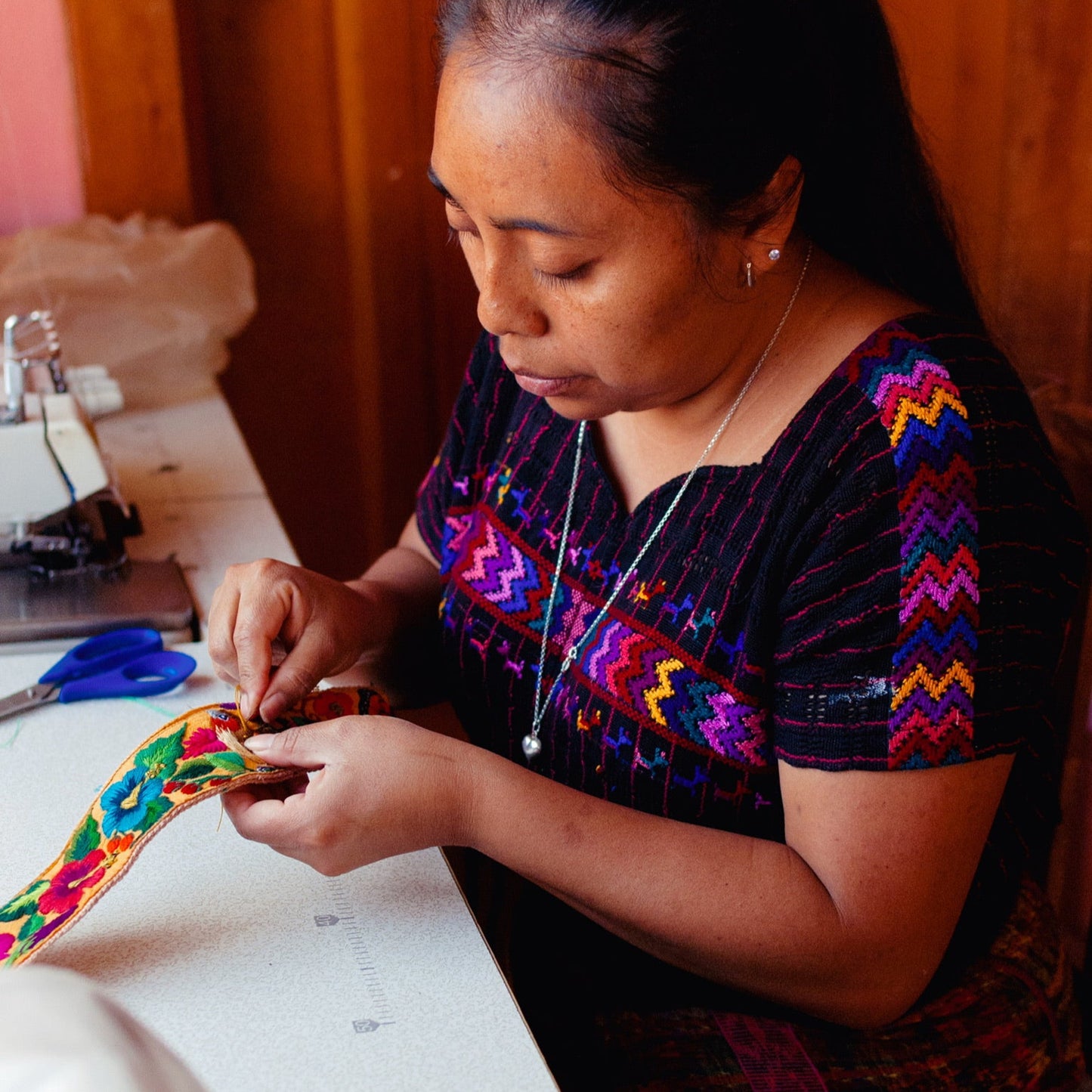 Woman in traditional clothing working on a colorful fabric item in a workshop.