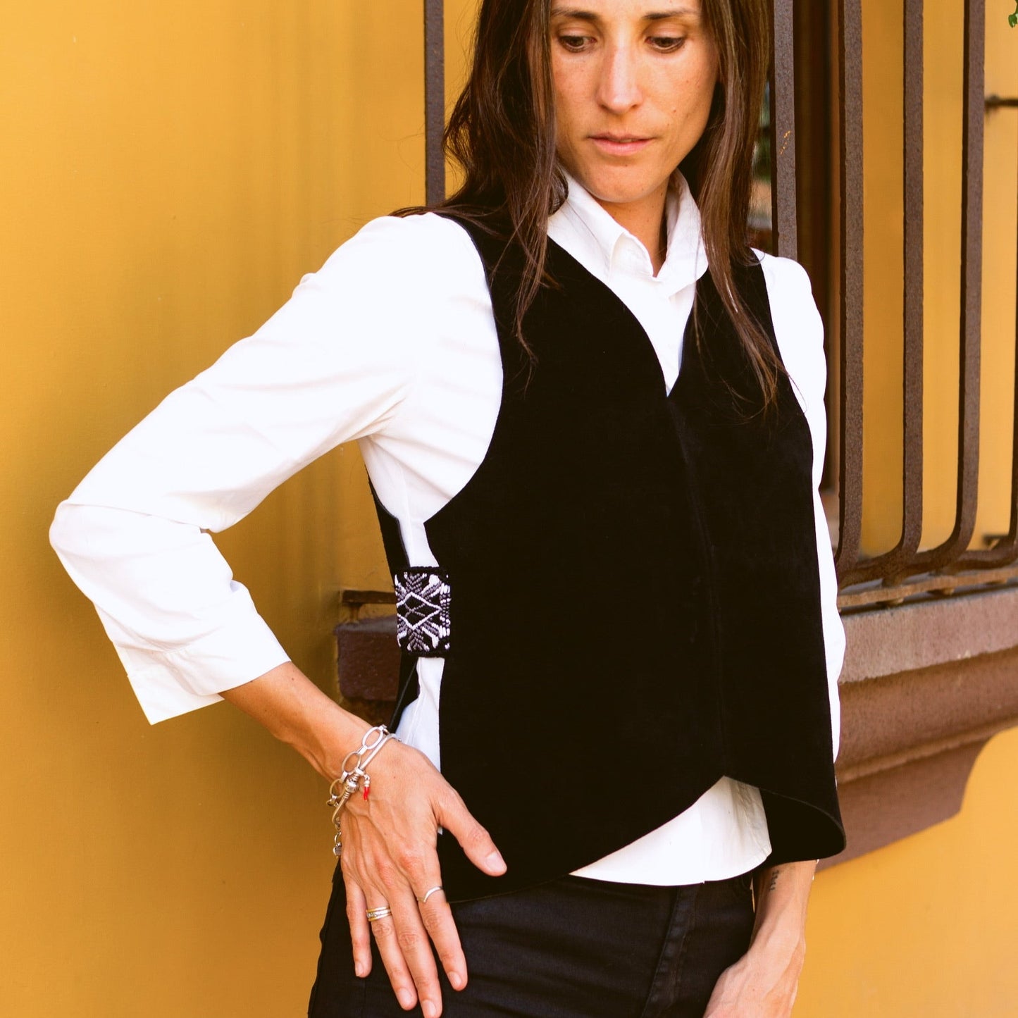 Woman wearing a black vest over a white shirt against a yellow wall.