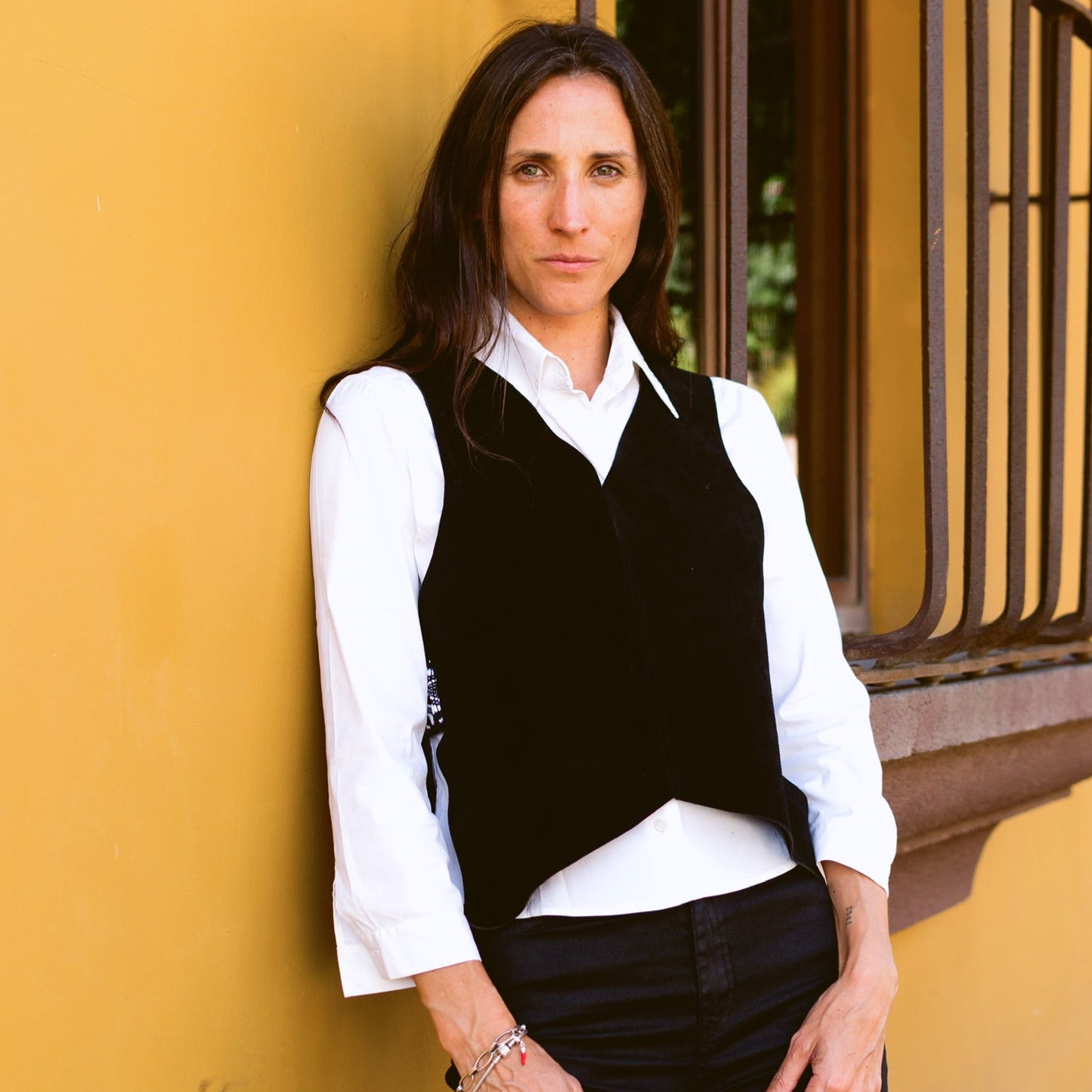 Woman wearing a black vest over a white shirt against a yellow wall.