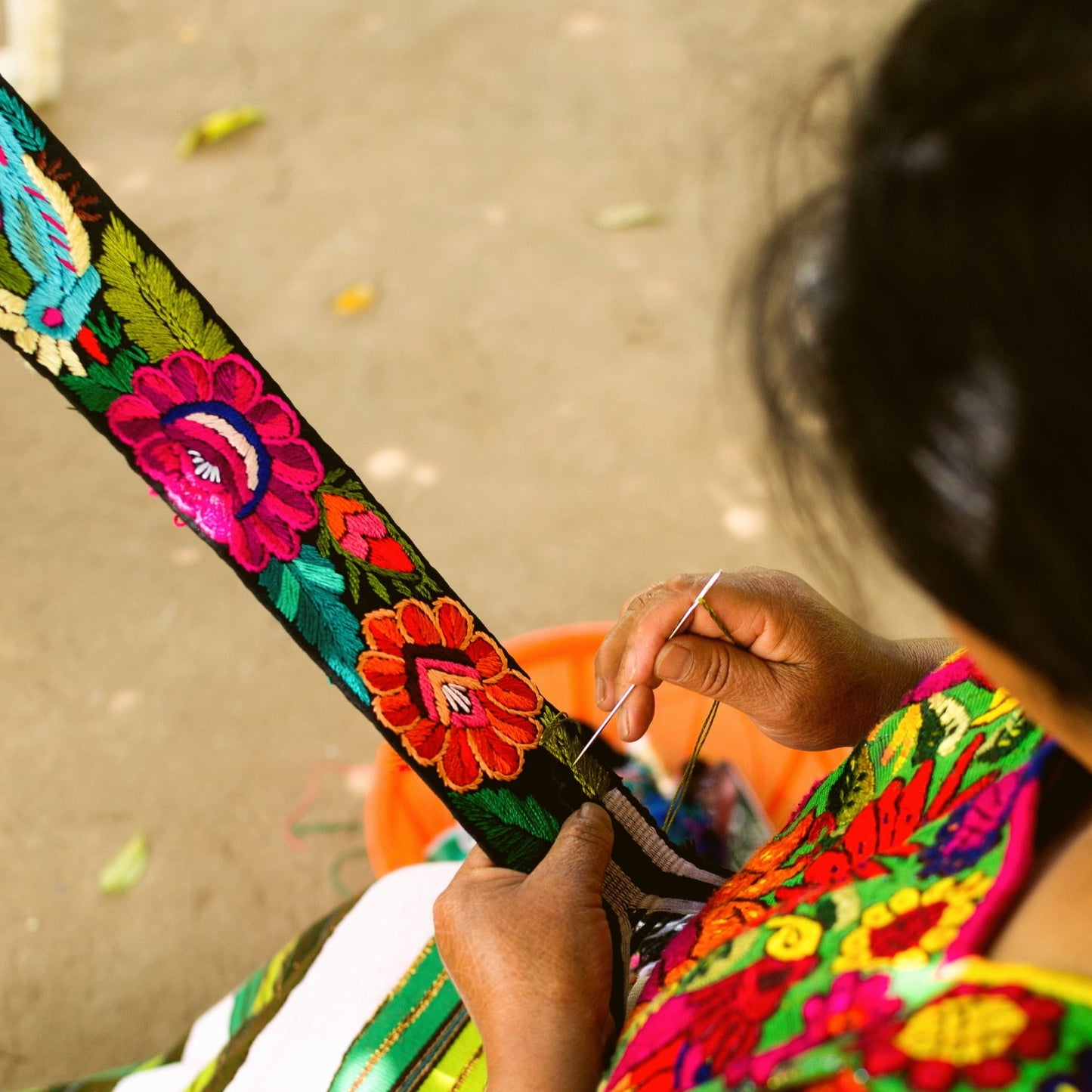 Person wearing a colorful embroidered garment with a close-up of their hand holding a needle and thread.