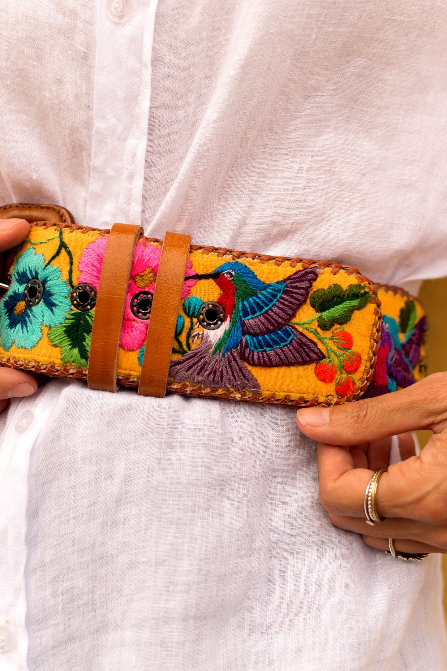 Colorful embroidered belt with birds and flowers held by a person wearing a white shirt.