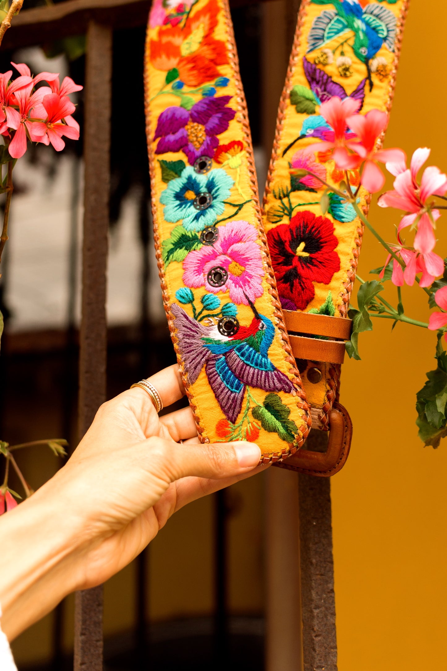 Colorful embroidered strap held by a hand with flowers in the background