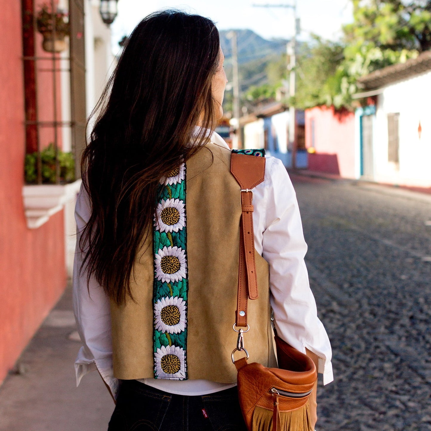 Woman walking down a street in a colorful village with a decorated bag.