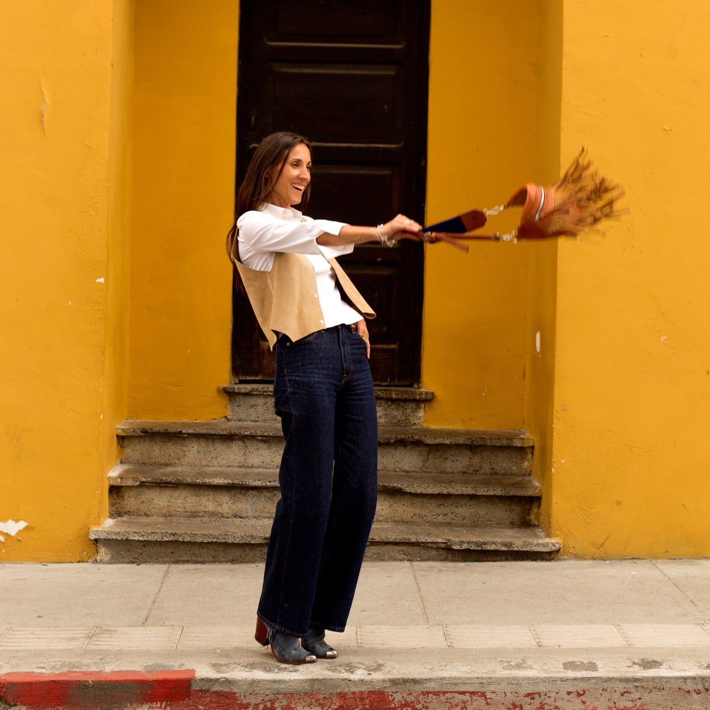 Woman holding a broom in front of a yellow wall with a dark door