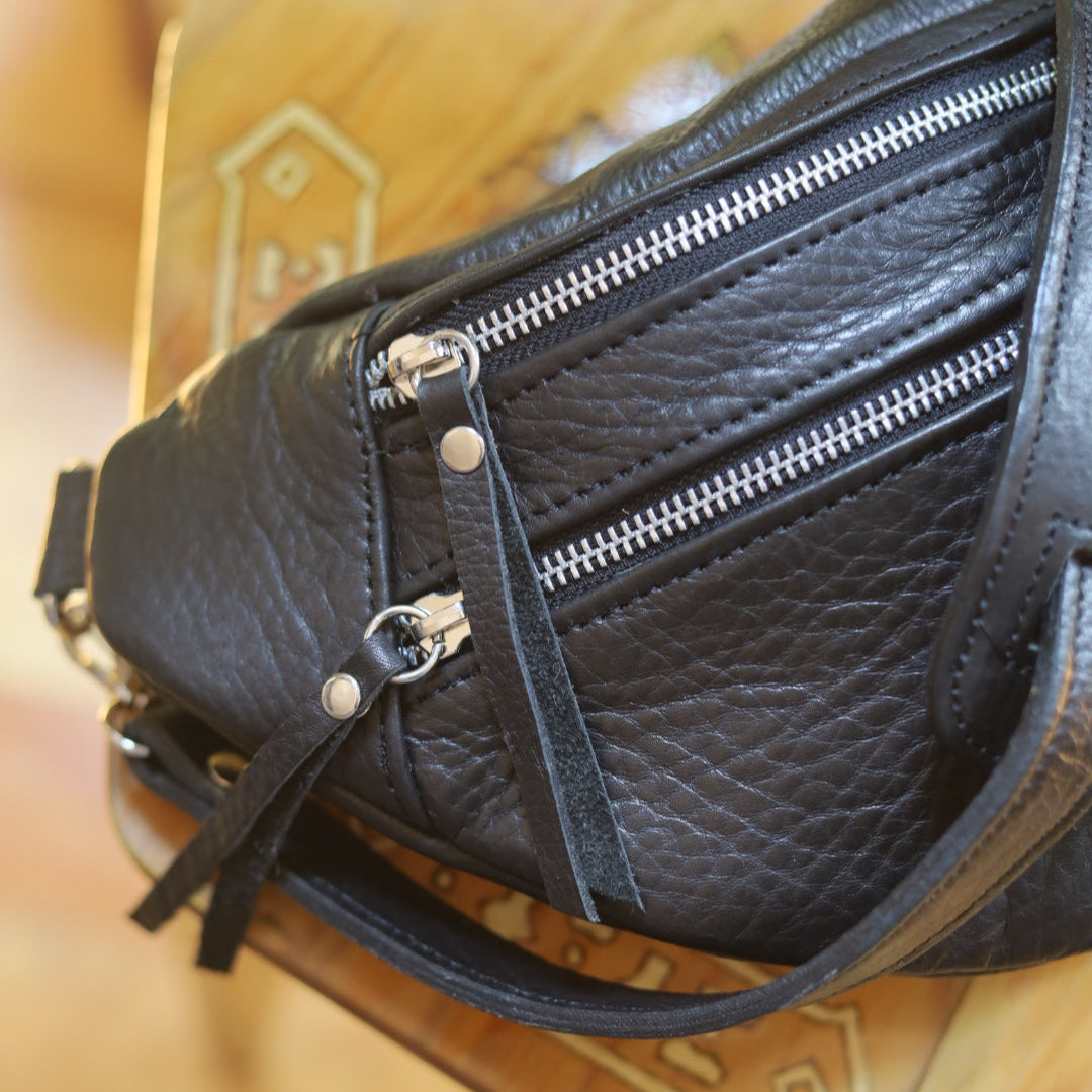 Black leather bag with zippers on a patterned surface