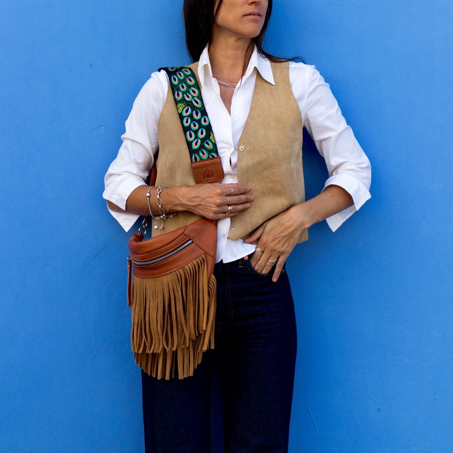 Woman holding a fringed bag against a blue wall