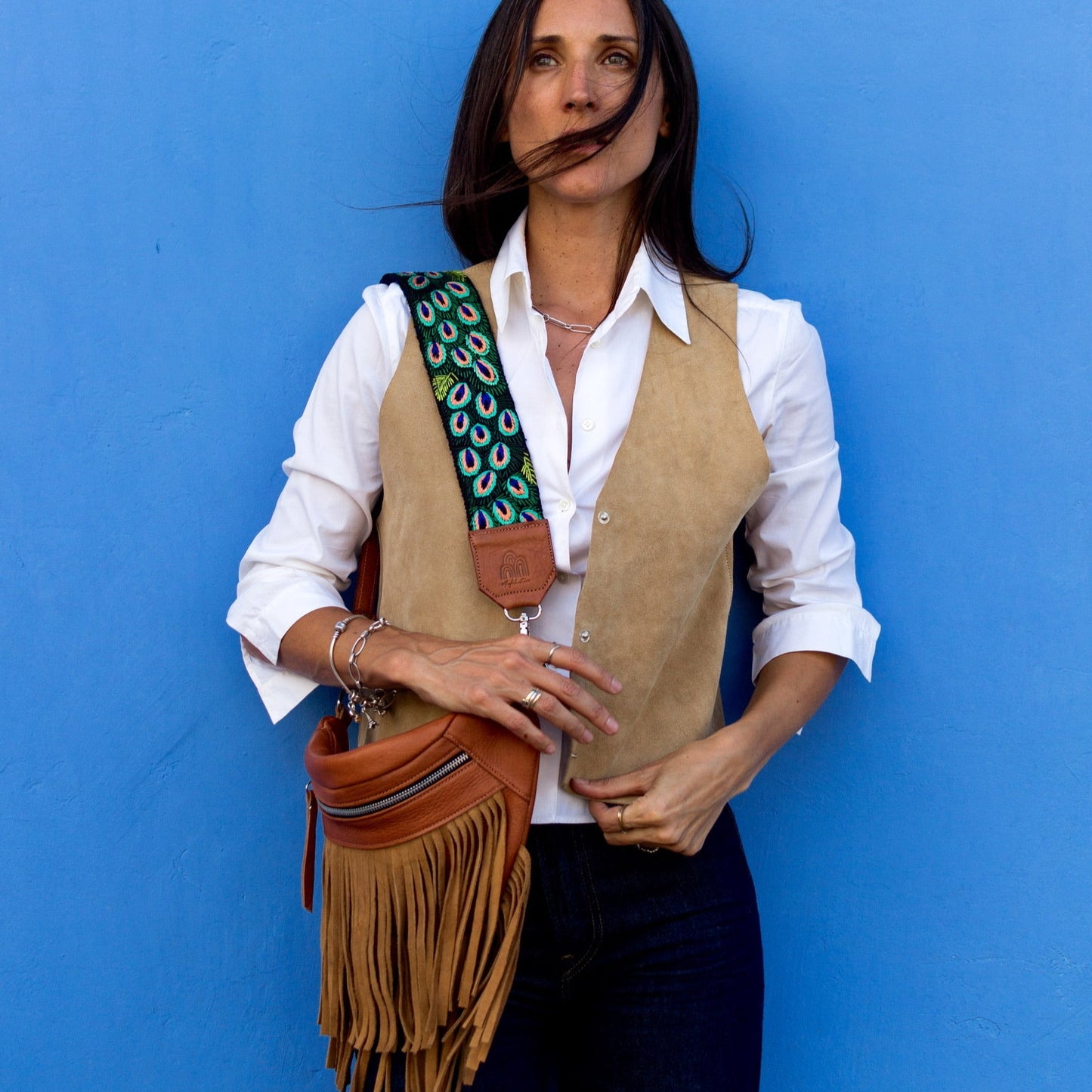 Woman holding a brown leather bag with a colorful strap against a blue background