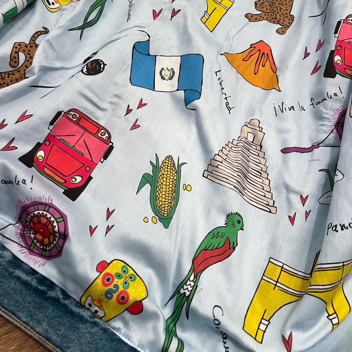 White fabric with colorful illustrations of a car, corn, pyramid, and other elements on a white background.