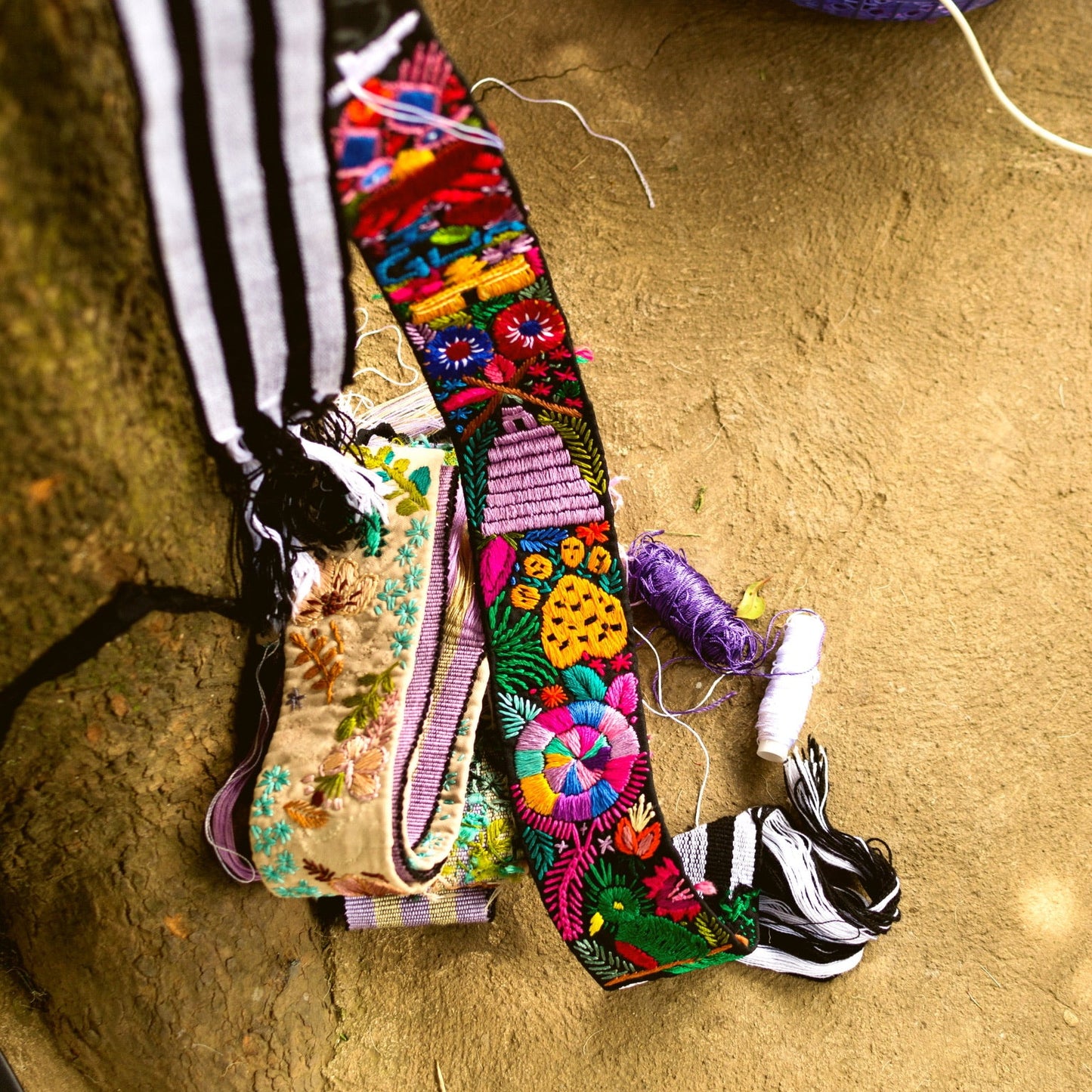 Colorful embroidered belt on a textured surface with a small container of items in the background.