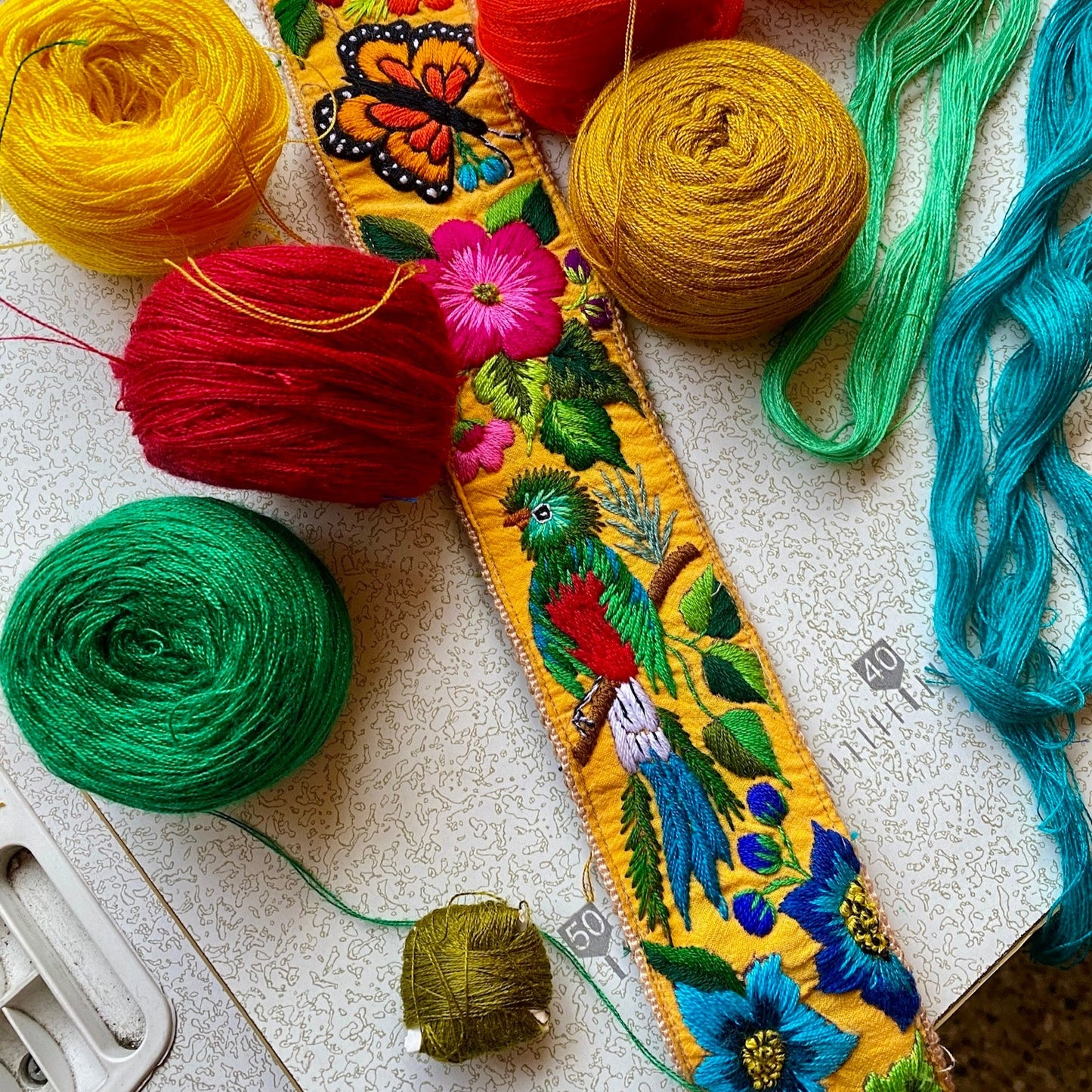 Colorful yarn skeins and embroidered fabric on a textured surface