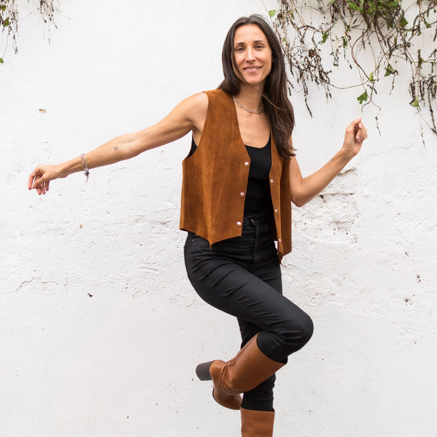 Woman wearing a brown vest and boots against a white wall.