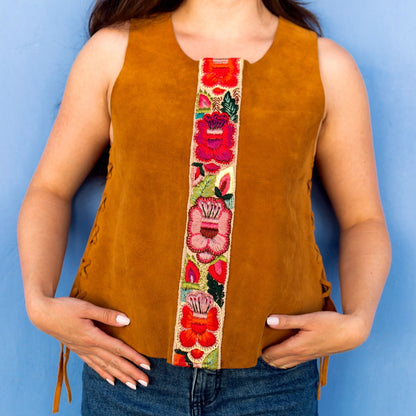 Woman wearing a mustard yellow sleeveless top with a colorful floral band against a blue background