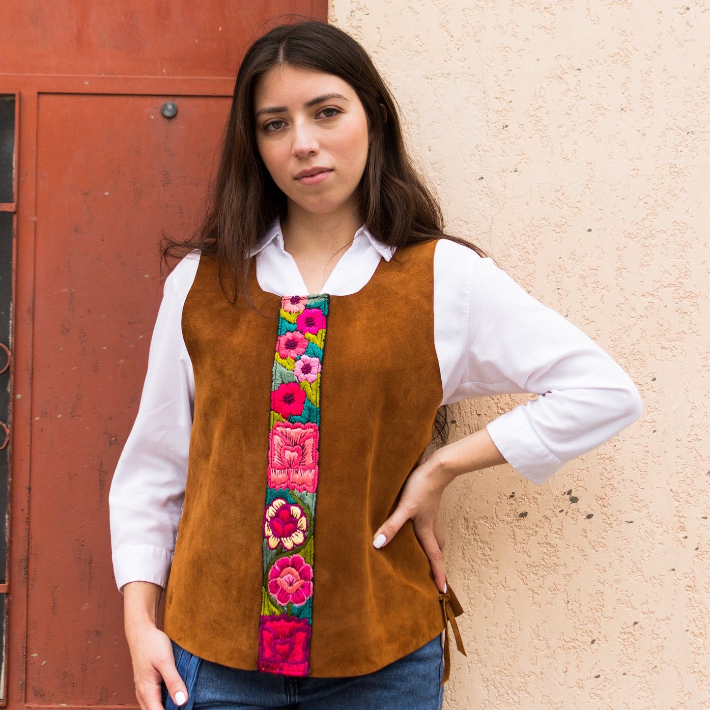 Woman wearing a brown vest with colorful floral patterns against a textured wall.