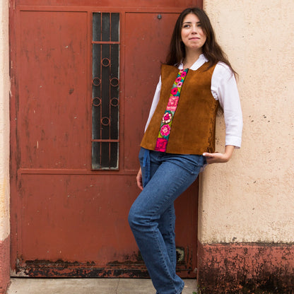 Woman wearing a brown vest with floral patterns leaning against a red door.