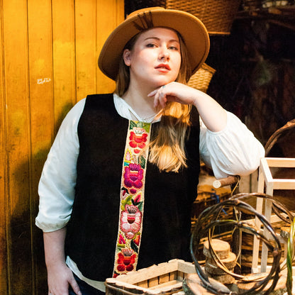 Woman wearing a straw hat and floral vest standing among woven baskets.