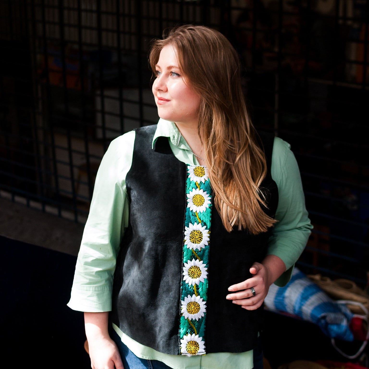 Woman wearing a black vest with a colorful floral pattern over a light green shirt.