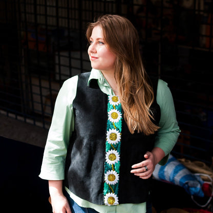 Woman wearing a black vest with a colorful floral pattern over a light green shirt.
