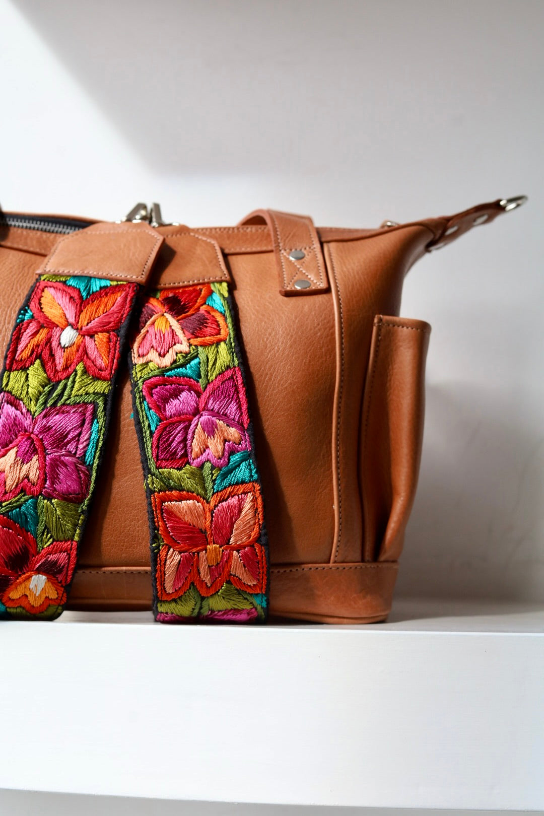 Brown leather handbag with colorful floral embroidery on a white background