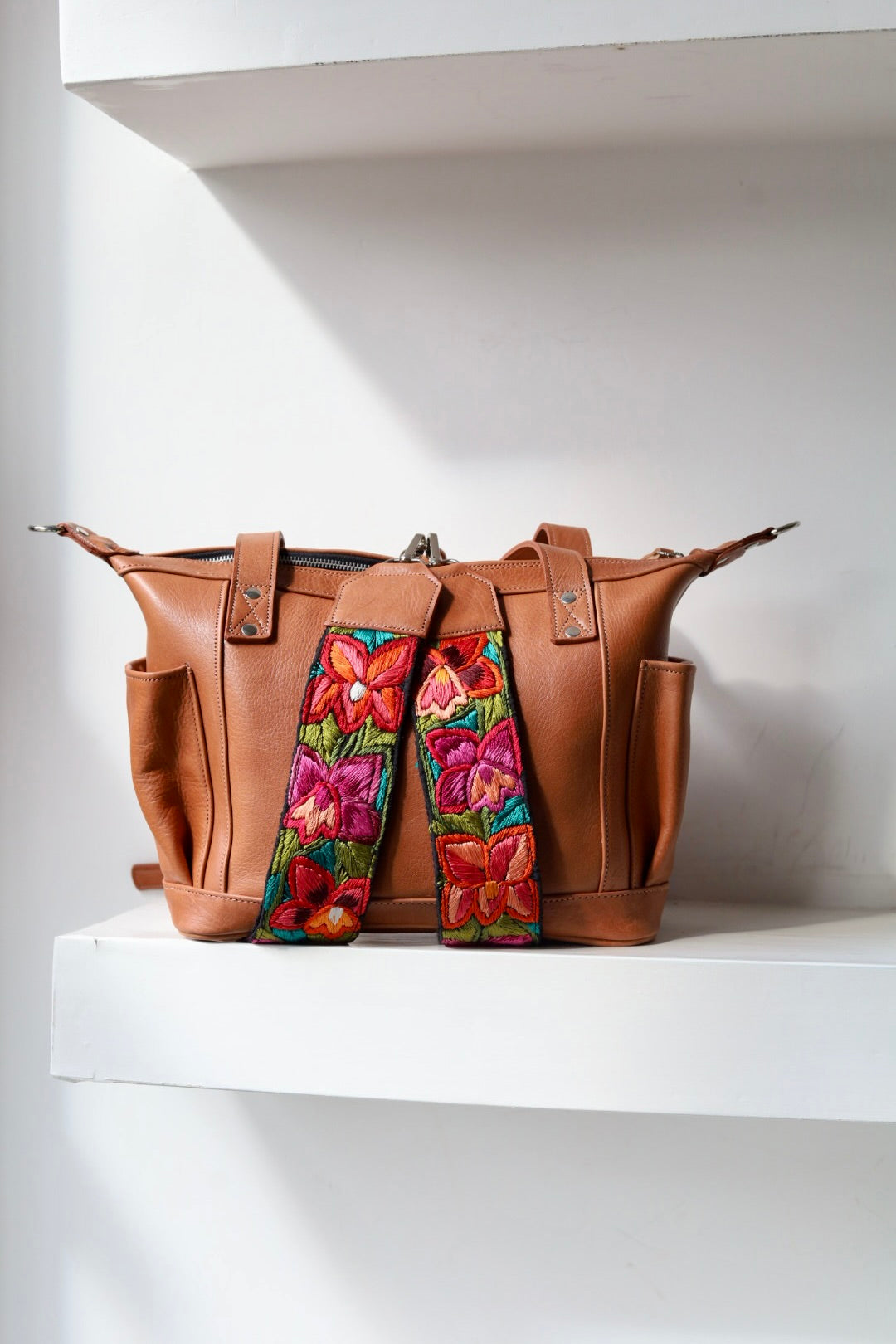 Brown leather bag with colorful floral embroidery on a white shelf