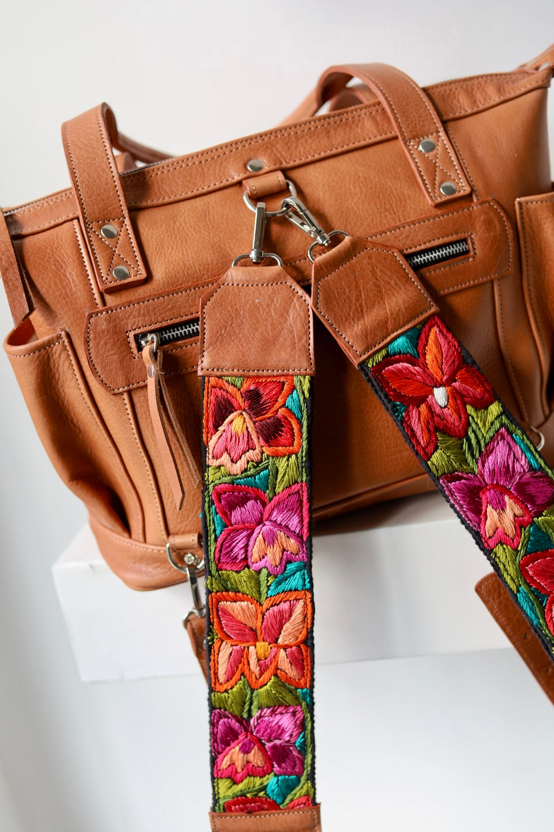 Brown leather bag with a colorful floral strap on a white background