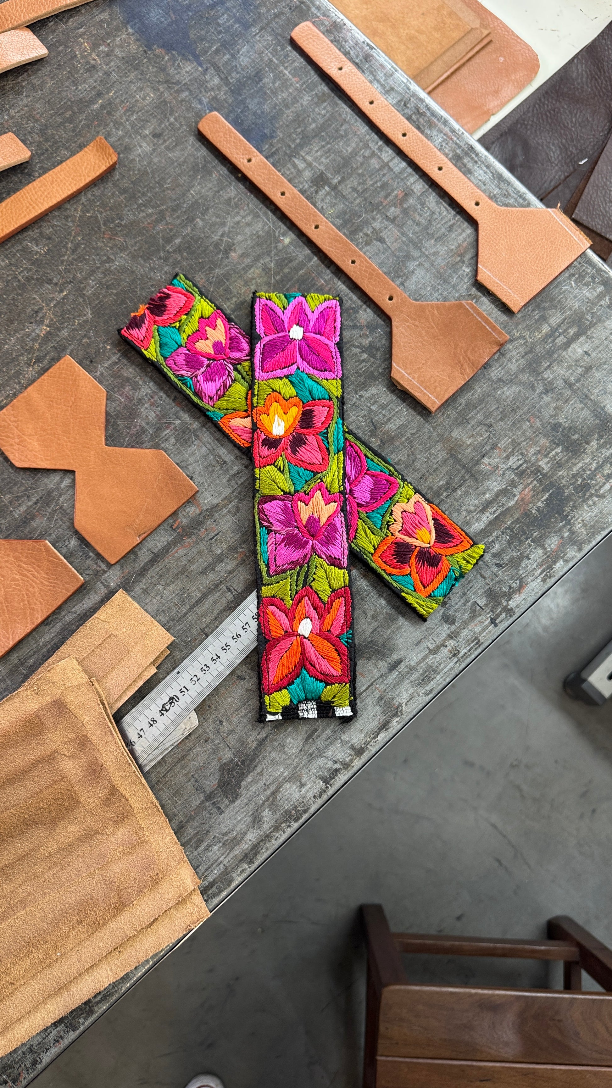 Colorful floral-patterned leather straps on a metal surface with leather pieces and a ruler.