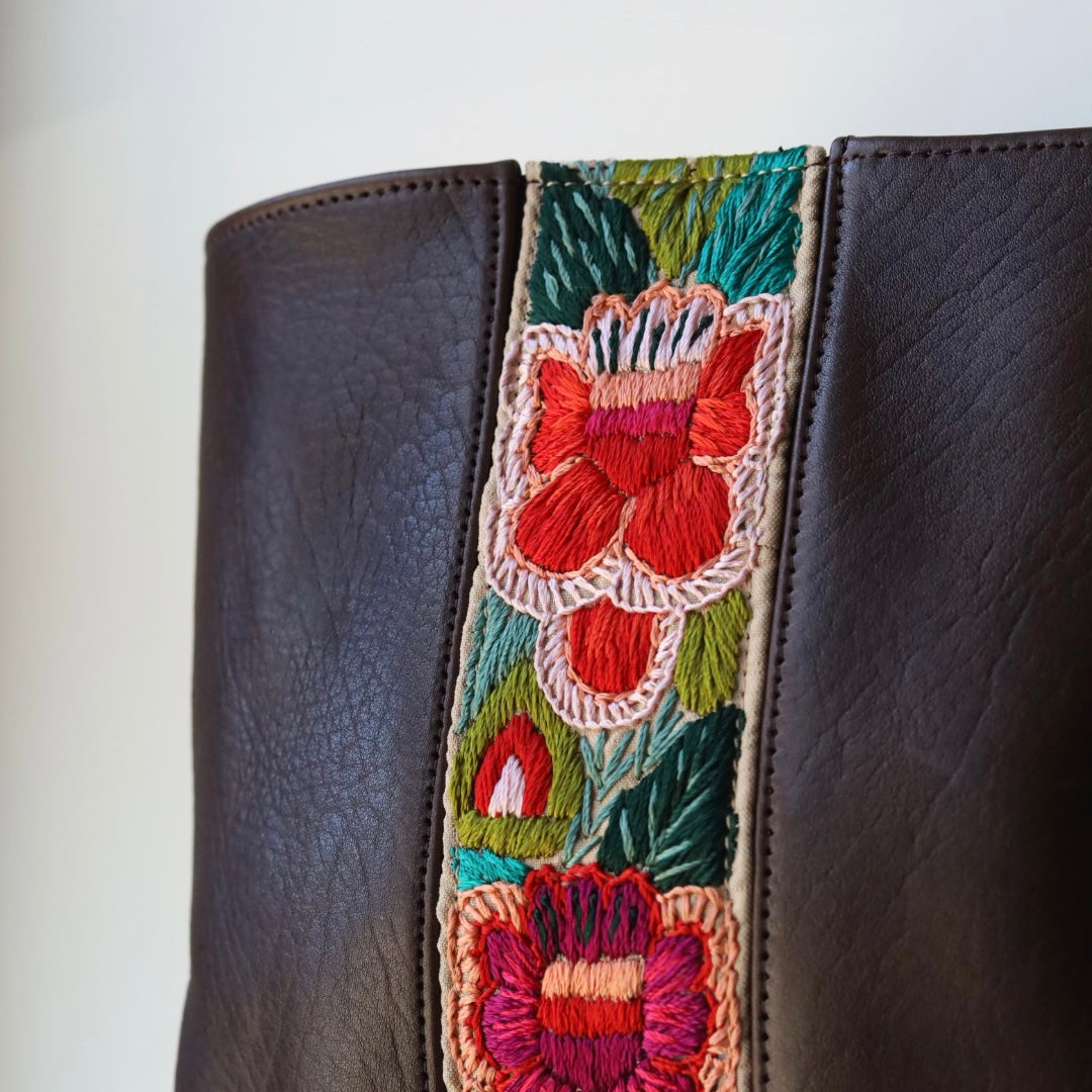 Brown leather bag with a colorful floral strap on a white background