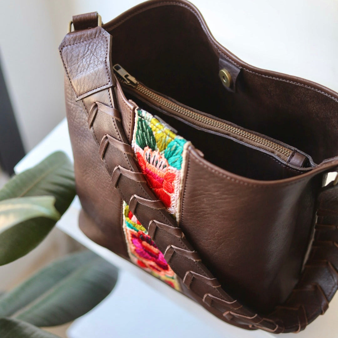 Brown leather handbag with colorful embroidered patches on a white surface.