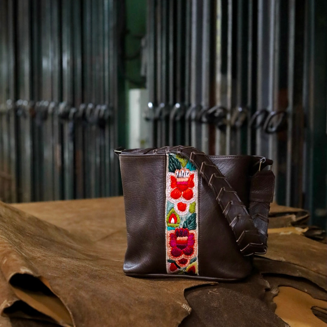 Brown leather bag with floral strap on a wooden surface