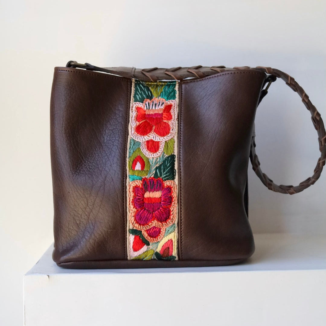 Brown leather handbag with a floral embroidered strap on a white background