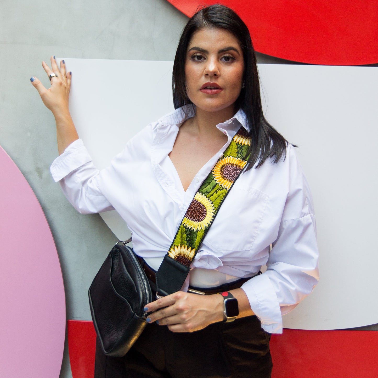 Woman holding a black handbag with a colorful strap against a colorful abstract wall.