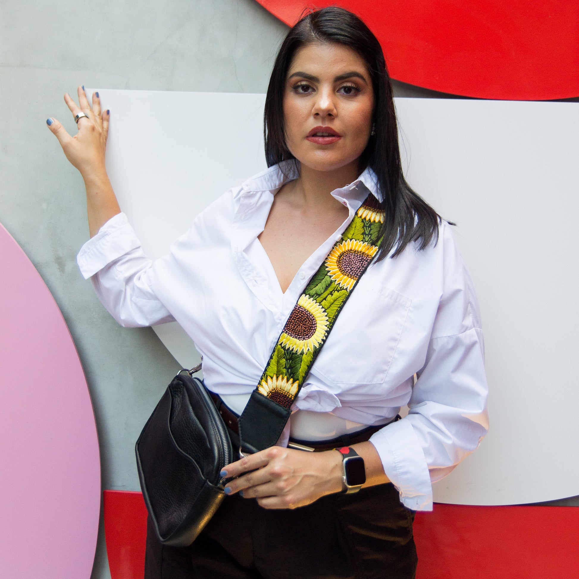 Woman holding a black handbag with a colorful strap against a colorful abstract wall.