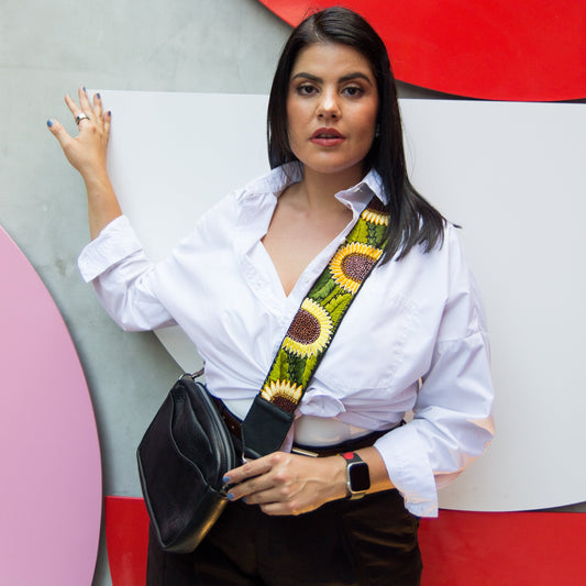 Woman holding a black handbag with a colorful strap against a colorful abstract wall.