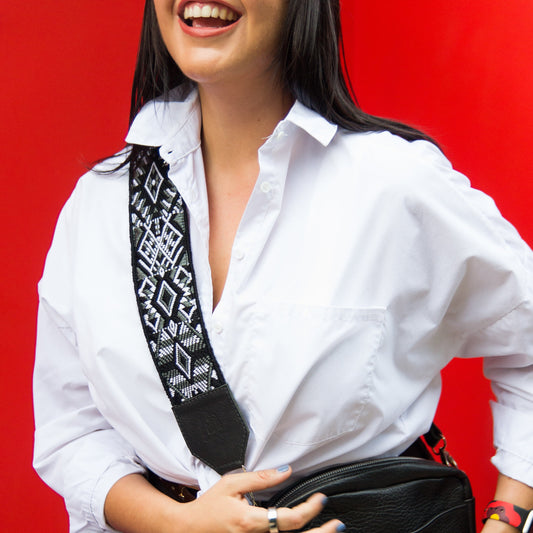 Person wearing a white shirt with a black and white patterned tie, holding a black bag against a red background.