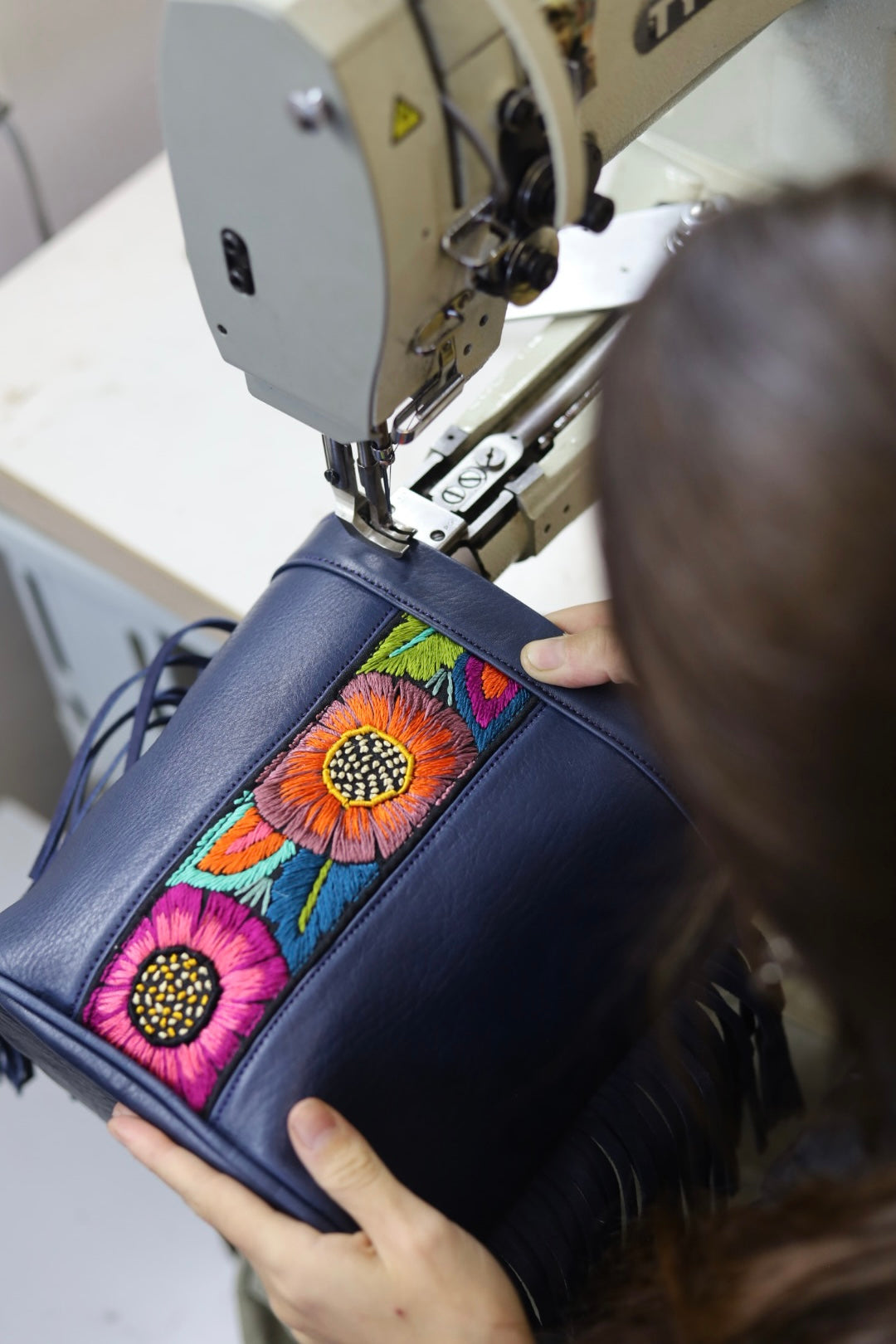 Person sewing a floral patch onto a blue bag using a sewing machine.
