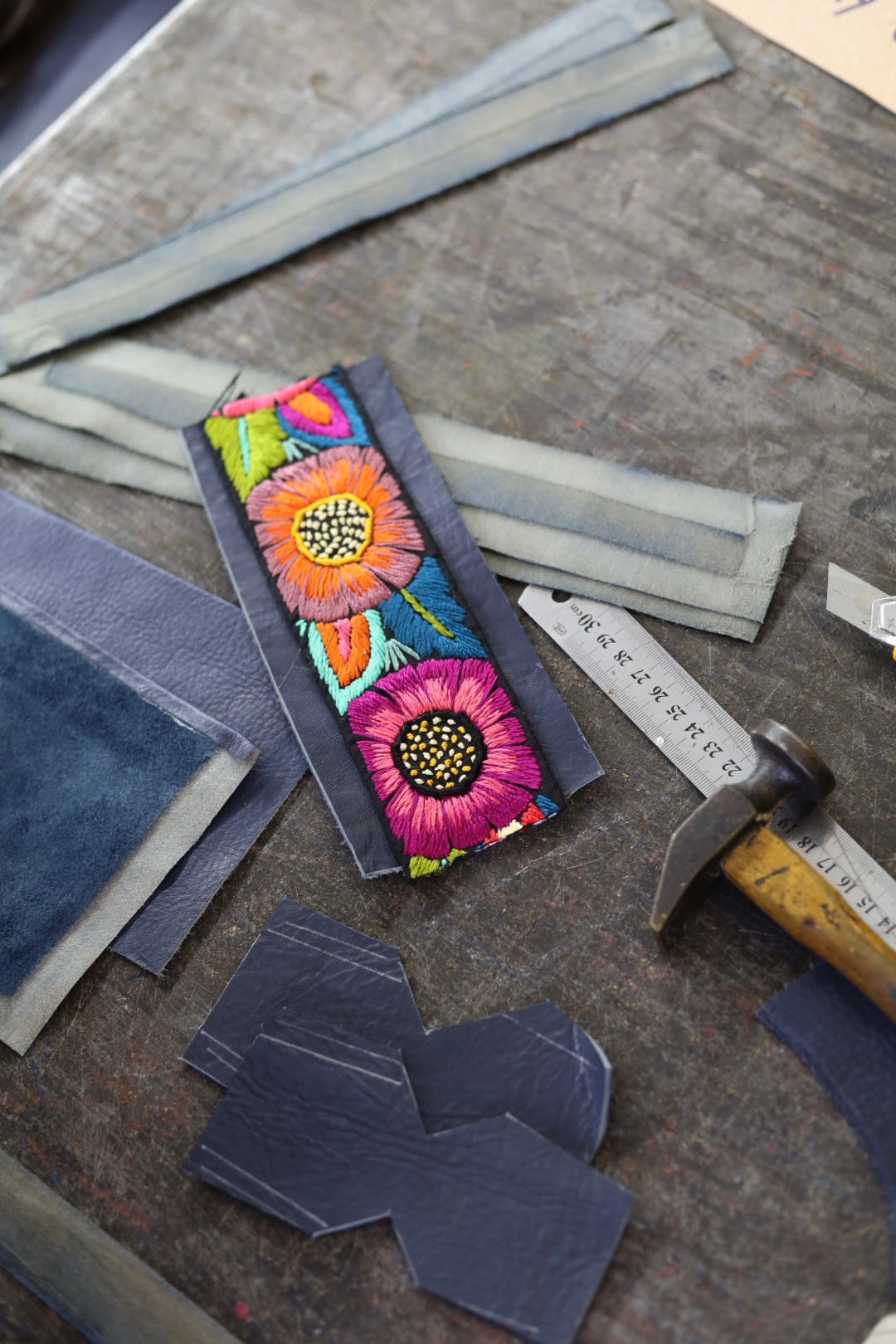 Colorful floral leather patch on a gray surface with leather scraps and a hammer.