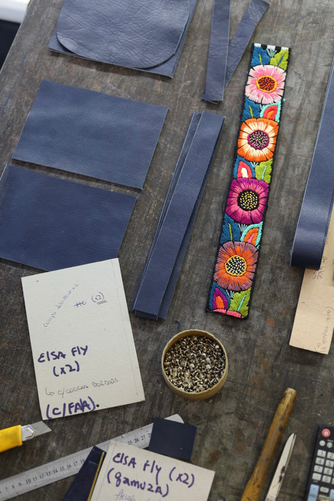 Workbench with leather pieces, a colorful floral-patterned strap, and various tools on a wooden surface.