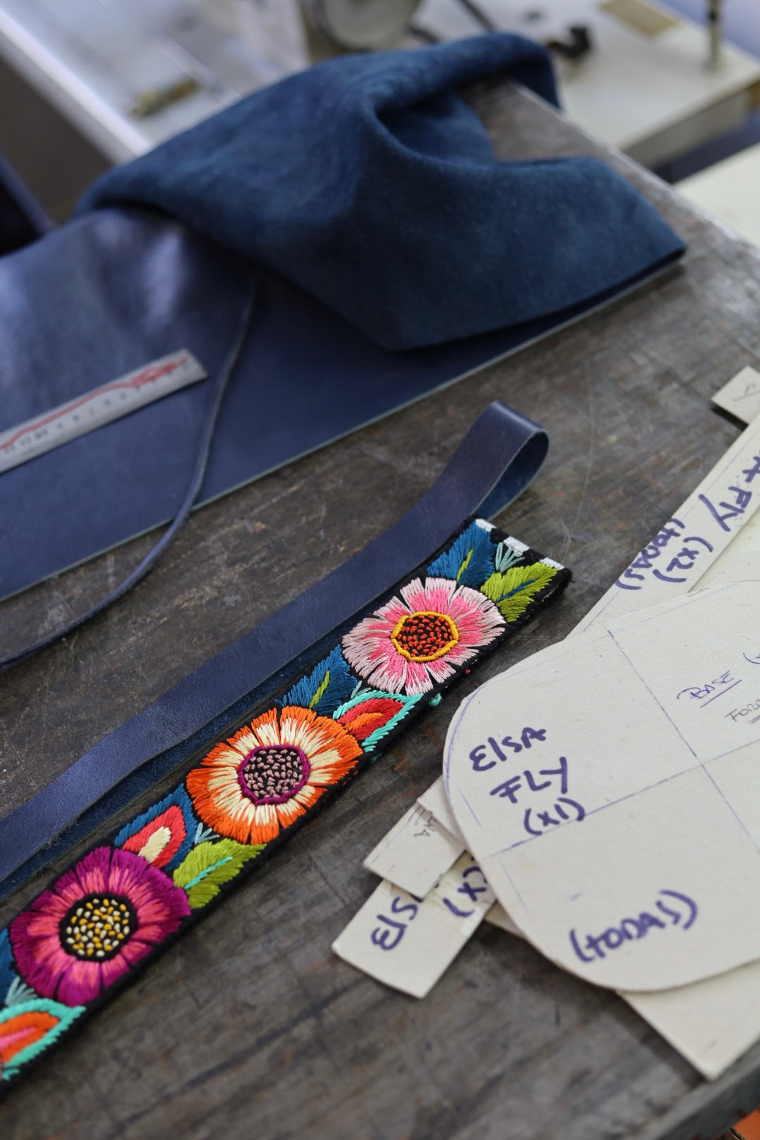 Embroidered floral strap on a wooden surface with fabric and labels.