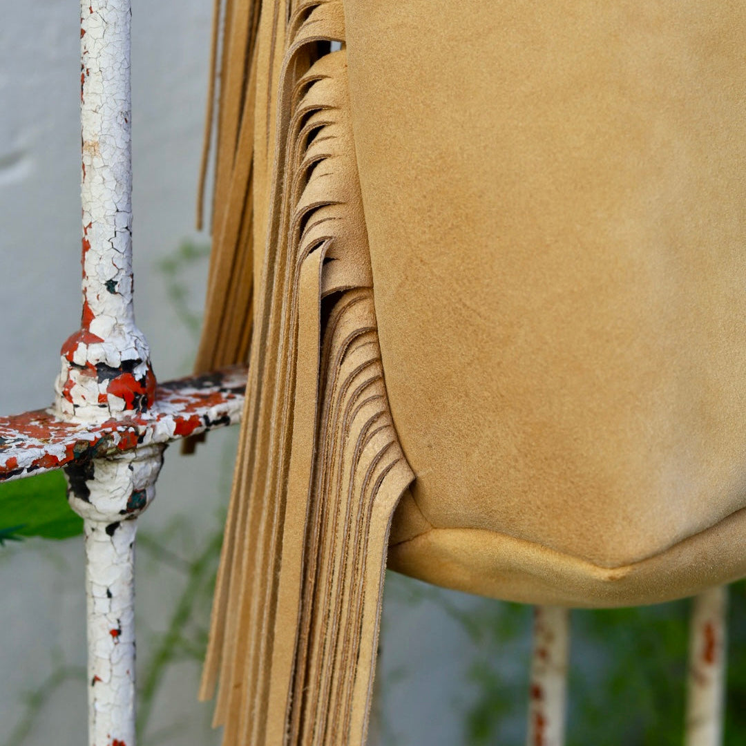 Close-up of a tan leather bag with fringes against a blurred background