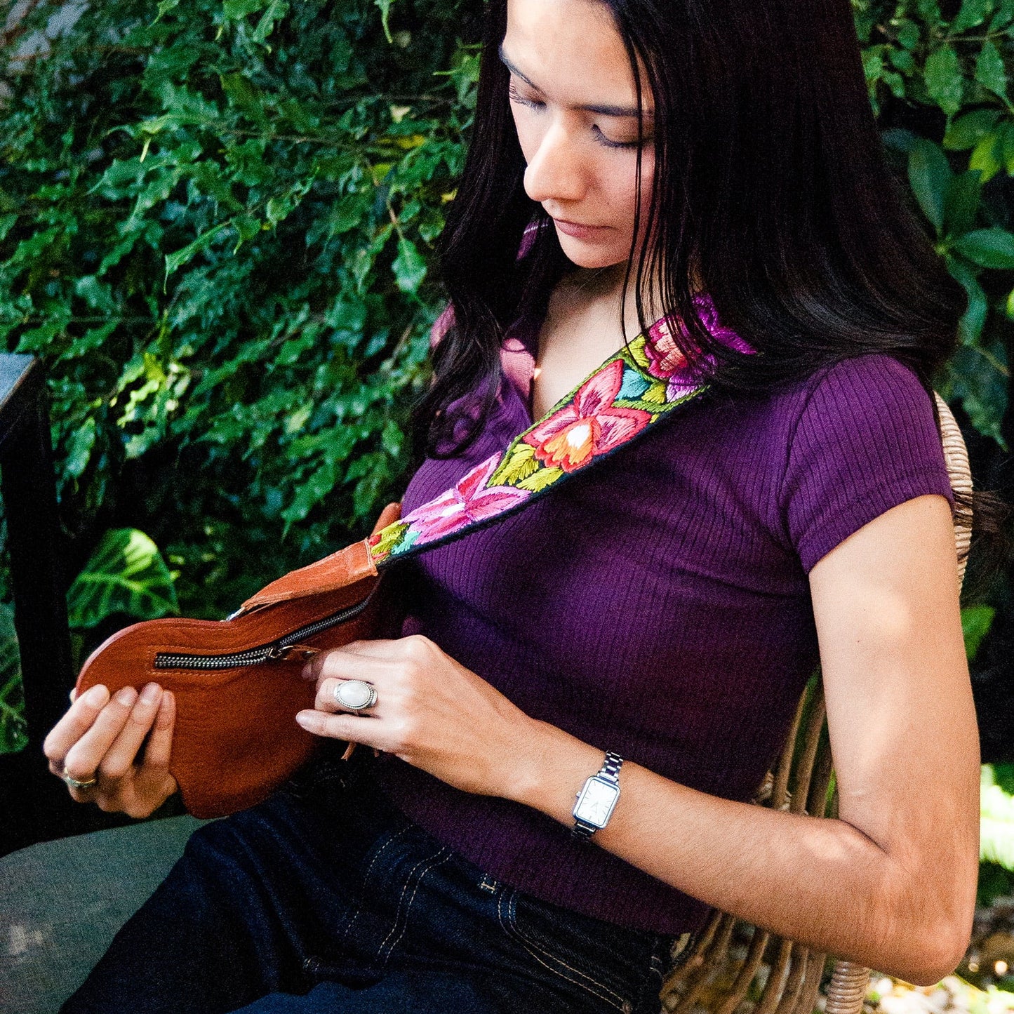 Woman playing a small stringed instrument outdoors with greenery in the background