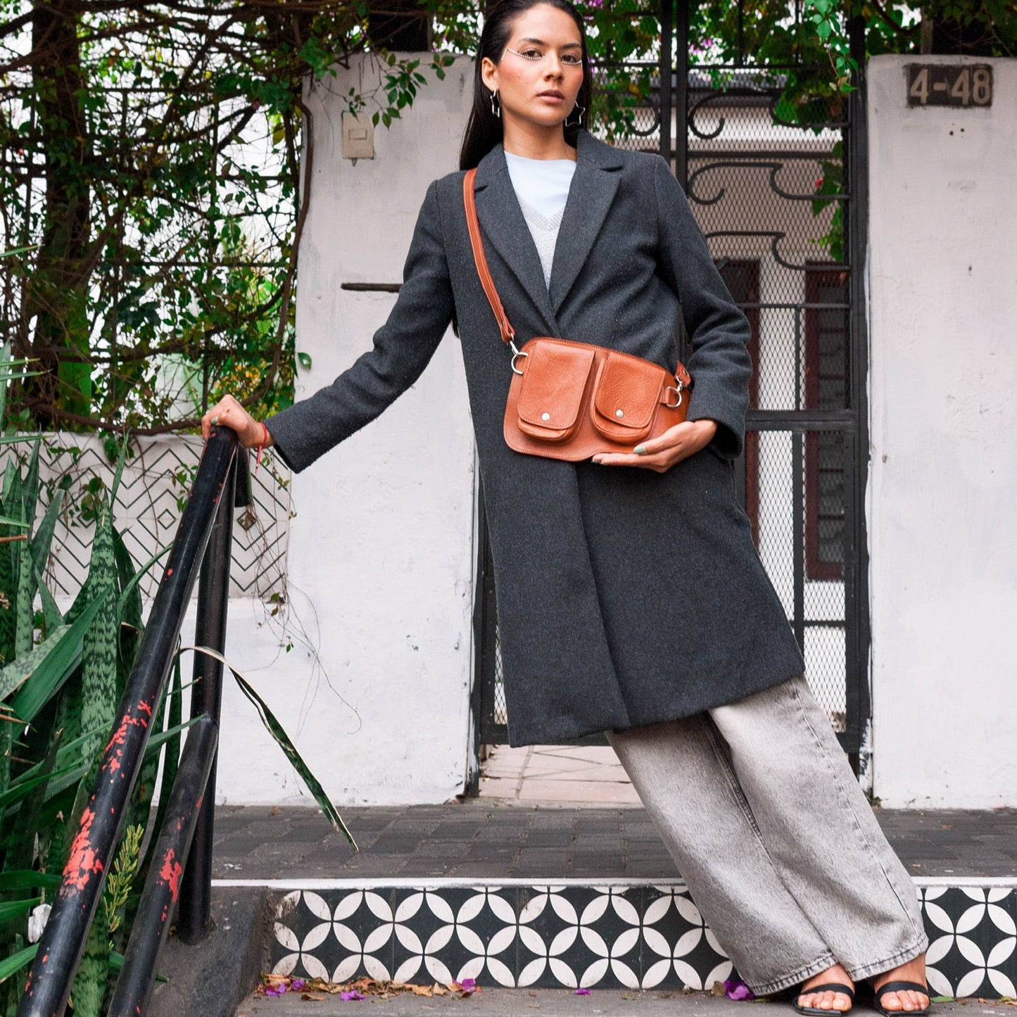 Woman in a gray coat with a brown leather bag standing on a decorative step.