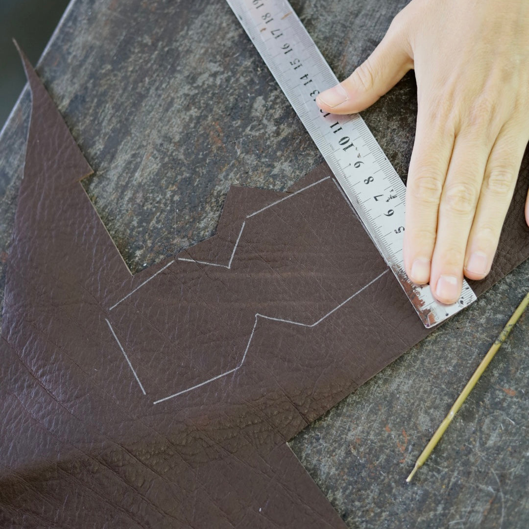 Person measuring and marking leather with a ruler and pencil